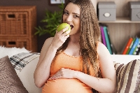 Pregnant woman eating apple on the sofa