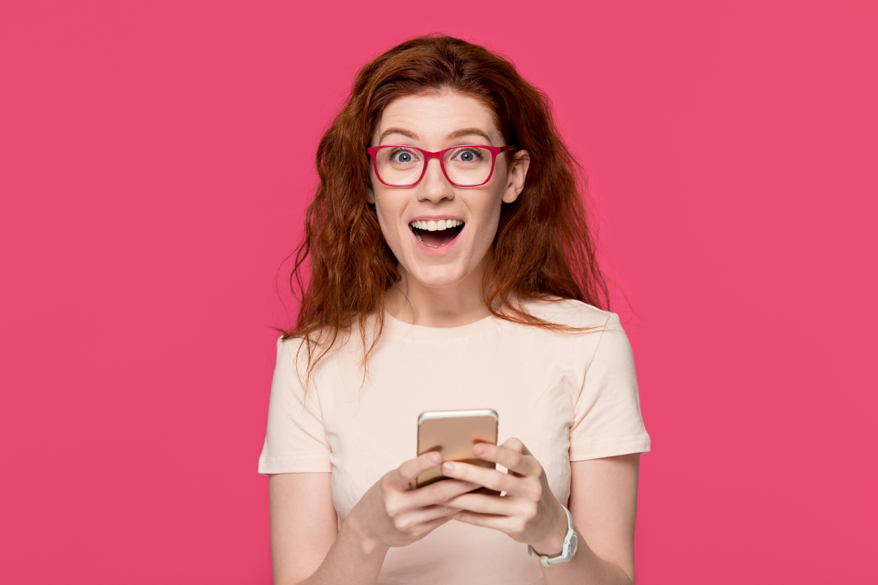 Excited redhead woman holding cell phone amazed by mobile win